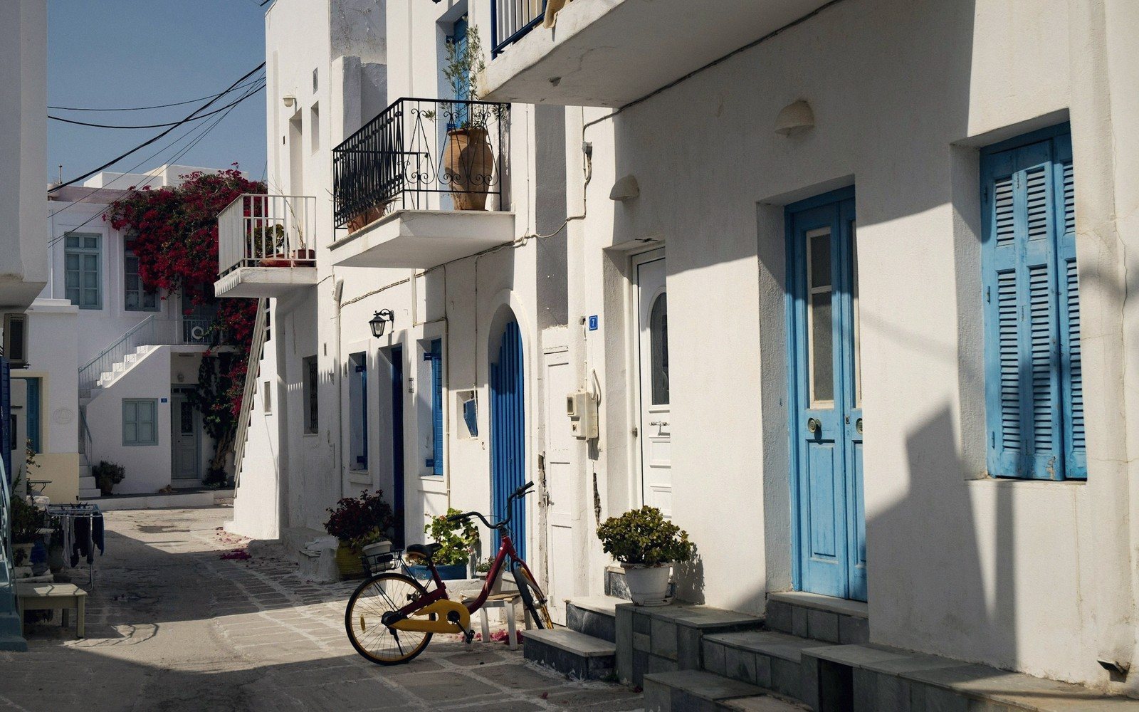 Whitewashed alley with blue doors and shutters, a parked bicycle, and flowering plants