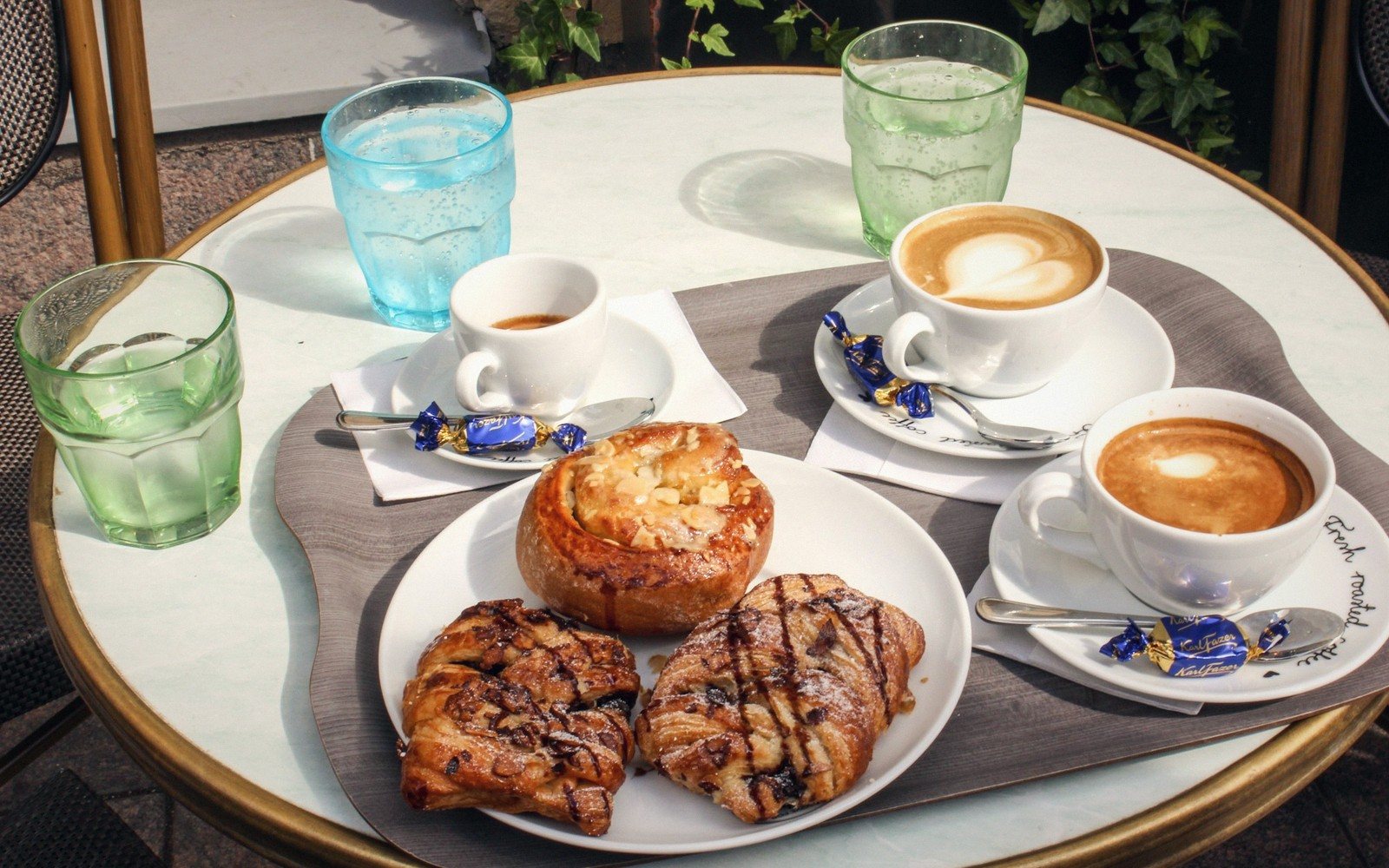 Outdoor café table with pastries, coffee cups, and glasses of sparkling water